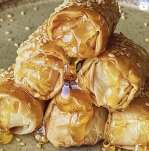 a photo of feta cheese bites stacked up, drizzled in honey and sprinkled with sesame seeds