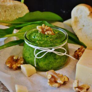 an image of white miso pesto in a short glass jar surrounded by walnut halves and cheese.