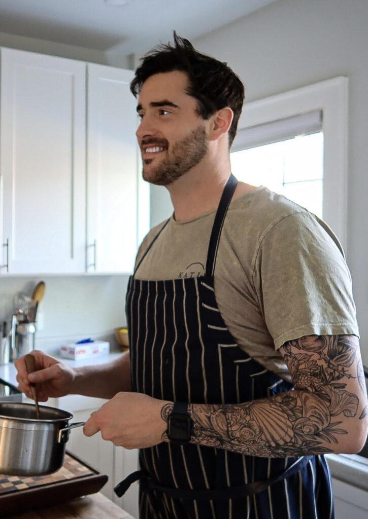 Image of founder Zack of Squier's Specialty Elixirs.  He's holding a pot with a spoon in it looking away from the camera.